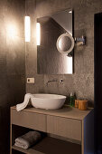 Washstand with countertop sink below mirror with infrared heating in bathroom with dark tiles