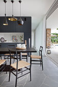 Schwarzer Esstisch mit Stühlen vor Raumteiler und offener Terrassentür