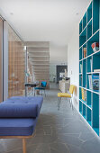 Turquoise fitted shelving and couch next to glass sliding door in open-plan interior