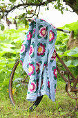Floral crocheted blanket draped over rusty bicycle in garden