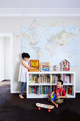 Girl and boy in children's room with bookshelf and map on wall