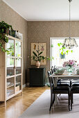 Set table in dining room with glass-fronted cabinet and vintage-style wallpaper