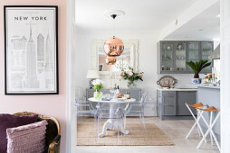 Open-plan kitchen with pale grey cupboards, round dining table and designer chairs with antique armchair and poster of New York in foreground