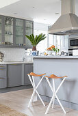 Pale grey counter and bar stools below extractor hood in open-plan kitchen