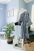 Kimono hung from free-standing mirror next to houseplant in bedroom with pale blue wall