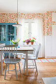 Spoke-back chairs around table in dining room with floral wallpaper