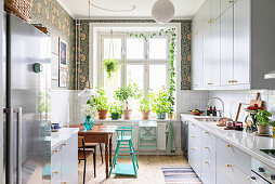 White cupboards and dark green patterned wallpaper in light-flooded kitchen
