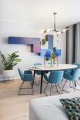 Oval dining table and blue chairs in open-plan interior with modular, wall-mounted cupboards