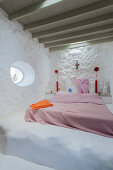 Doppelbett mit rosa Tagesdecke in ländlichem Schlafzimmer mit weiß getünchter Wand
