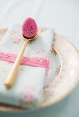 Pink egg on gold spoon and napkin on plate