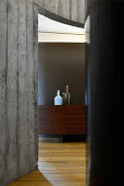 View of wooden sideboard through doorway in curved concrete wall