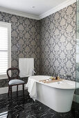 Free-standing bathtub in bathroom with patterned wallpaper and marble floor tiles