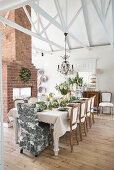 Festively set dining table in front of brick fireplace in high-ceilinged room
