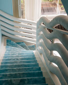 Staircase with sky-blue runner and white, sculptural balustrade