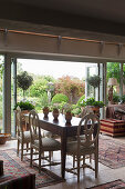 Dining table and antique chairs in front of open terrace doors in English country house