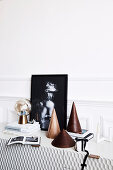 Cone-shaped decorative objects, books, table lamp and black and white photography on a sideboard