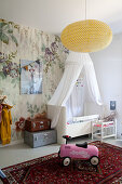 Canopy over cot in nursery with floral wallpaper