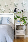 Houseplant on bedside table next to bed against lilac-patterned wallpaper