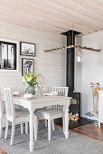 Dining table against board wall and wood-burning stove with row of pegs around stove pipe