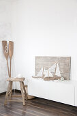 Sailing boat ornaments made from driftwood and fabric remnants next to stool and paddles in corner