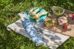 Hand-sewn cutlery roll, plate of honeydew melon and open-faced sandwiches on board