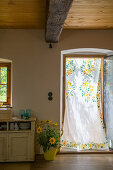 Mit Blumen bemalter Vorhang in der offenen Tür zum Landhaus