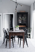 Black display cabinet, wooden dining table and bistro chairs in interior with grey walls