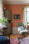 Armchair and standard lamp next to corner cabinet in interior with salmon-pink walls