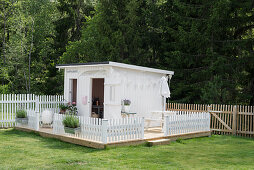 White playhouse with fence on platform in garden