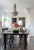 Black dining table and wooden chairs below vintage chandelier in dining area