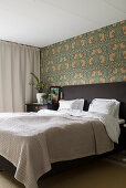 Double bed against wall with William Morris wallpaper