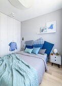 Cushions in shades of blue on double bed, bedside table and fitted wardrobes in bedroom
