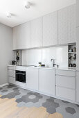 Pale grey kitchen cabinets in open-plan interior with two different floor coverings
