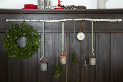 Candle lanterns made from tin cans and wreath of conifer branches hung from birch branch