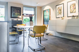 Offener Essbereich mit rundem Tisch, Freischwinger, Hängeschrank und Kunstwerken an den Wänden