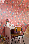 Old chair and small pink table against red floral wallpaper