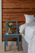 Blue chair used as bedside table next to bed against wooden bedroom wall