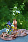 Kupferdrahtrollen und sommerliche Wiesenblumensträußchen auf Tisch im Freien
