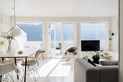 Dining table, sofa and large windows overlooking balcony in light-flooded interior