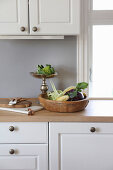 Rustic wooden bowl and vegetables on silver cake stand in kitchen