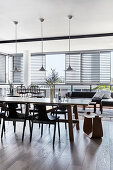 Long dining table and chairs below pendant lamps with outdoor lounge in background