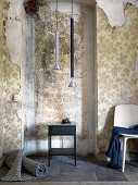 Rolled rug, side table, pendant lamps and chair in room with peeling wallpaper