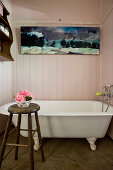 Vintage Badewanne, darüber Gemälde an holzverkleideter Wand im Bad, im Vordergrund Hocker mit Blumenschale