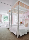 Zwei weiße Pfostenbetten mit Schabracken in Schlafzimmer mit zartrosa Wänden und Vorhängen