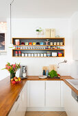 Kitchen counter with wooden worksurface below crockery on shelves