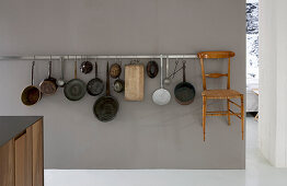 Kochgeschirrsammlung und filigraner Holzstuhl an grauer Wand