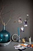 Branch in turquoise demijohn on desk against grey wall