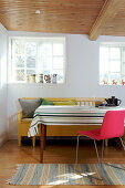 Gestreifte Tischdecke überm Tisch mit pinkem Stuhl und gelber Bank im Esszimmer
