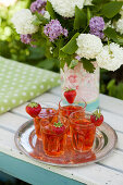 Erdbeeren an Trinkgläsern mit Erdbeersirup-Getränk vorm Blumenstrauß