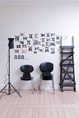 Schwarze Designerstühle, Studioleuchte und Leiter vor einer Bilderwand